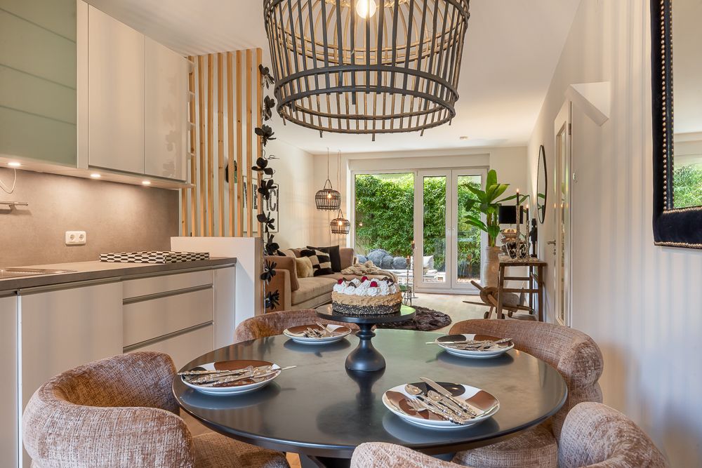 Essbereich mit rundem Tisch und Kuchenteller, dahinter offenes Wohnzimmer mit Gartenzugang.