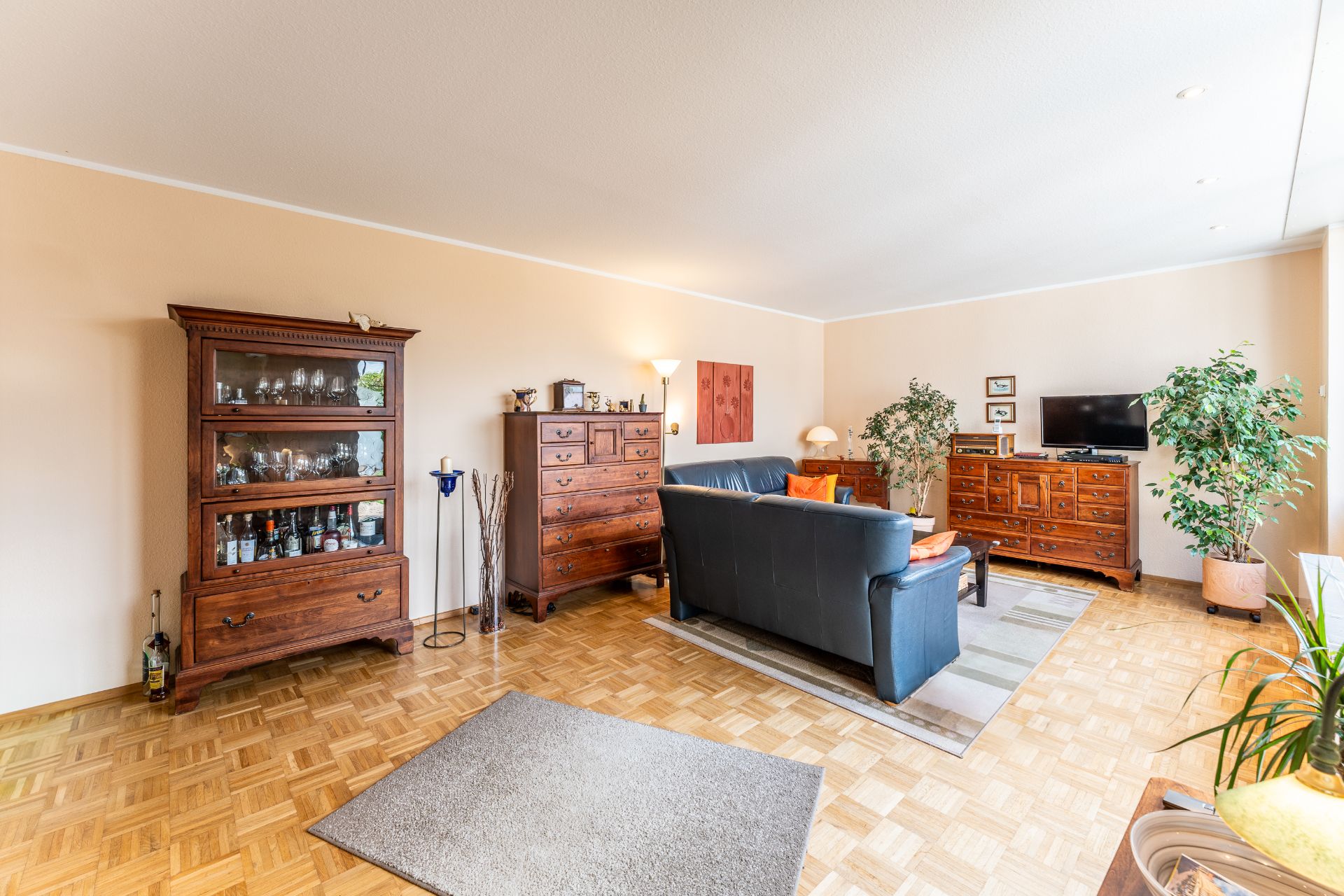 Helles Wohnzimmer mit Parkettboden, blauer Couch, Holzmöbeln und Zimmerpflanzen.
