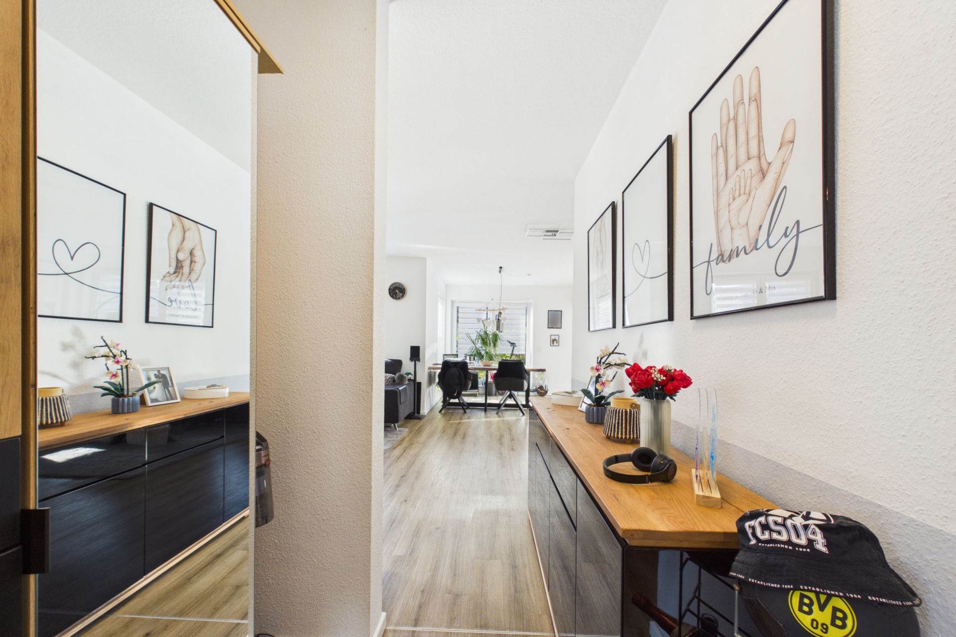 Heller Flur mit Holzkommode, Bildern an der Wand und Blick ins Wohnzimmer.