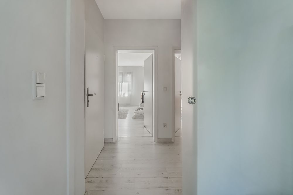 Heller Flur mit offenen Türen und Blick in ein weiteres Zimmer mit Fenster.
