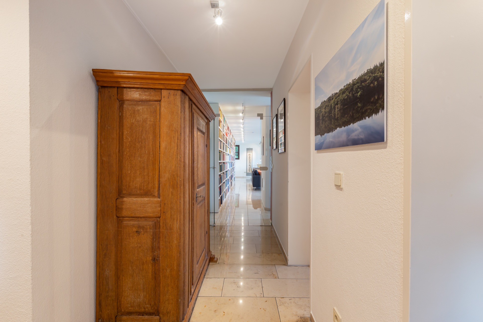 Heller Flur mit Holzschrank, Fliesenboden und Wandbild, Regal im Hintergrund.