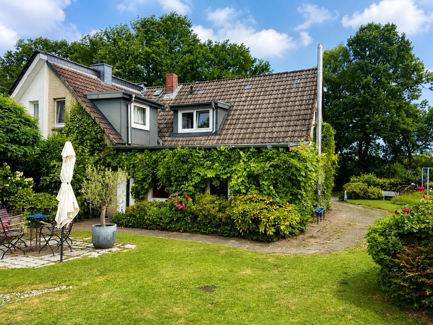 Haus mit begrüntem Garten, Terrasse, Gartenmöbeln und Kletterpflanzen an der Fassade.