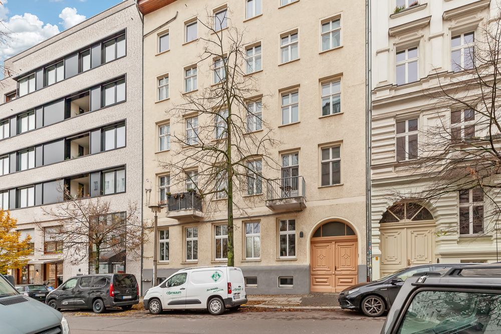 Mehrstöckiges Wohnhaus mit beigen Fassaden, Balkonen und parkenden Autos auf der Straße.