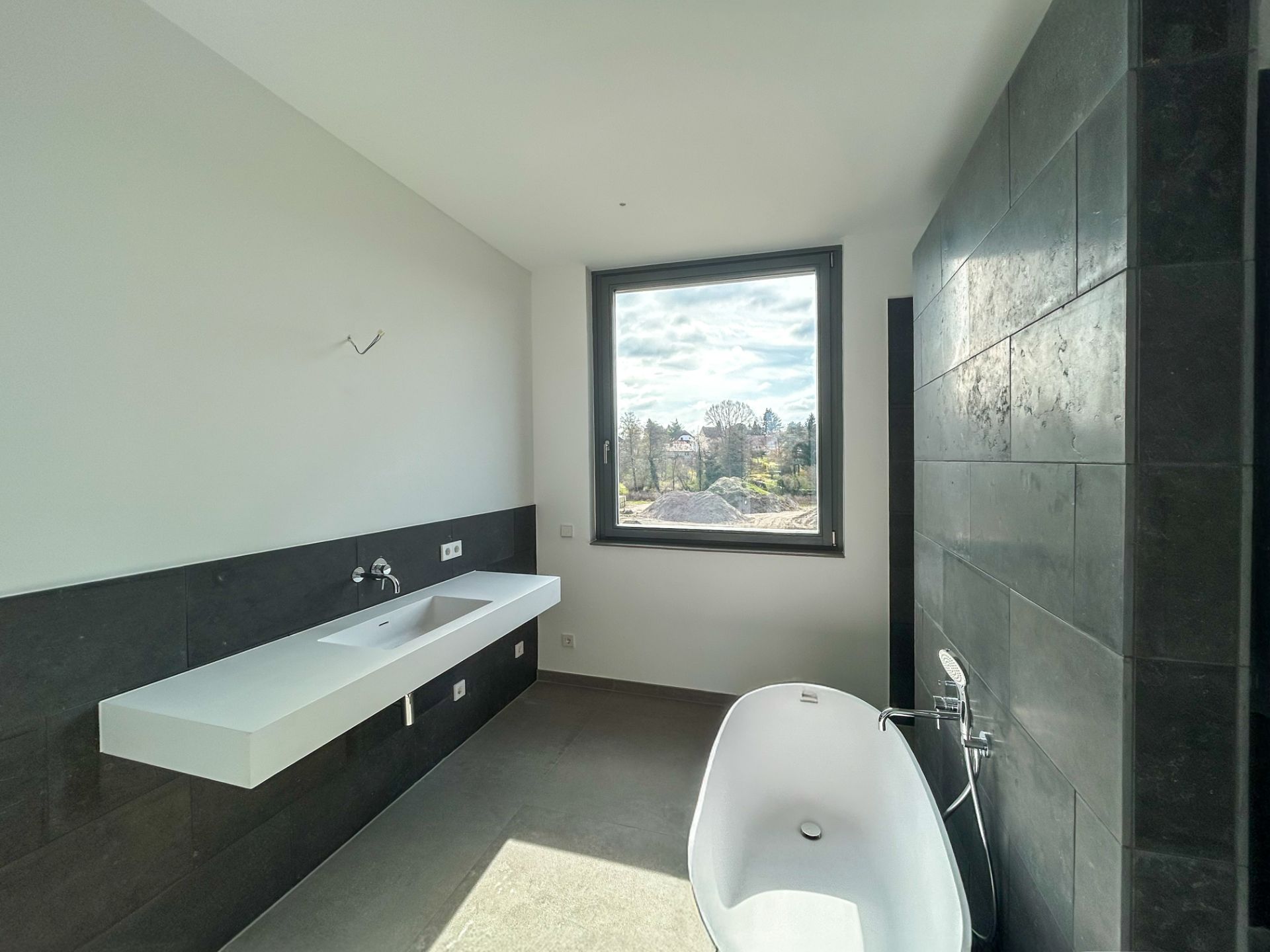 Modernes Badezimmer mit freistehender Badewanne, großem Waschbecken und Fenster mit Ausblick.