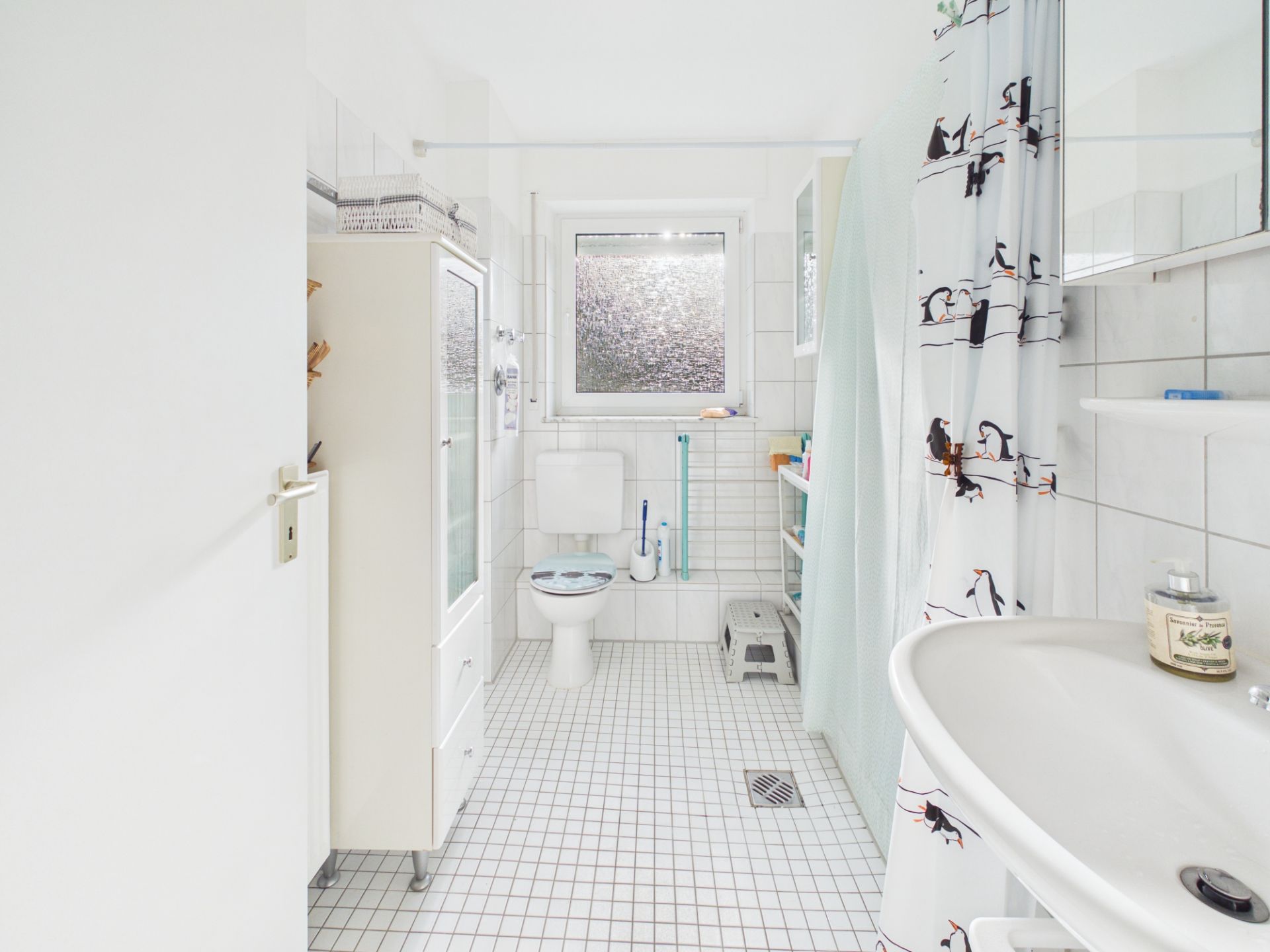 Helles Badezimmer mit Toilette, Waschbecken, Duschvorhang und Fenster.