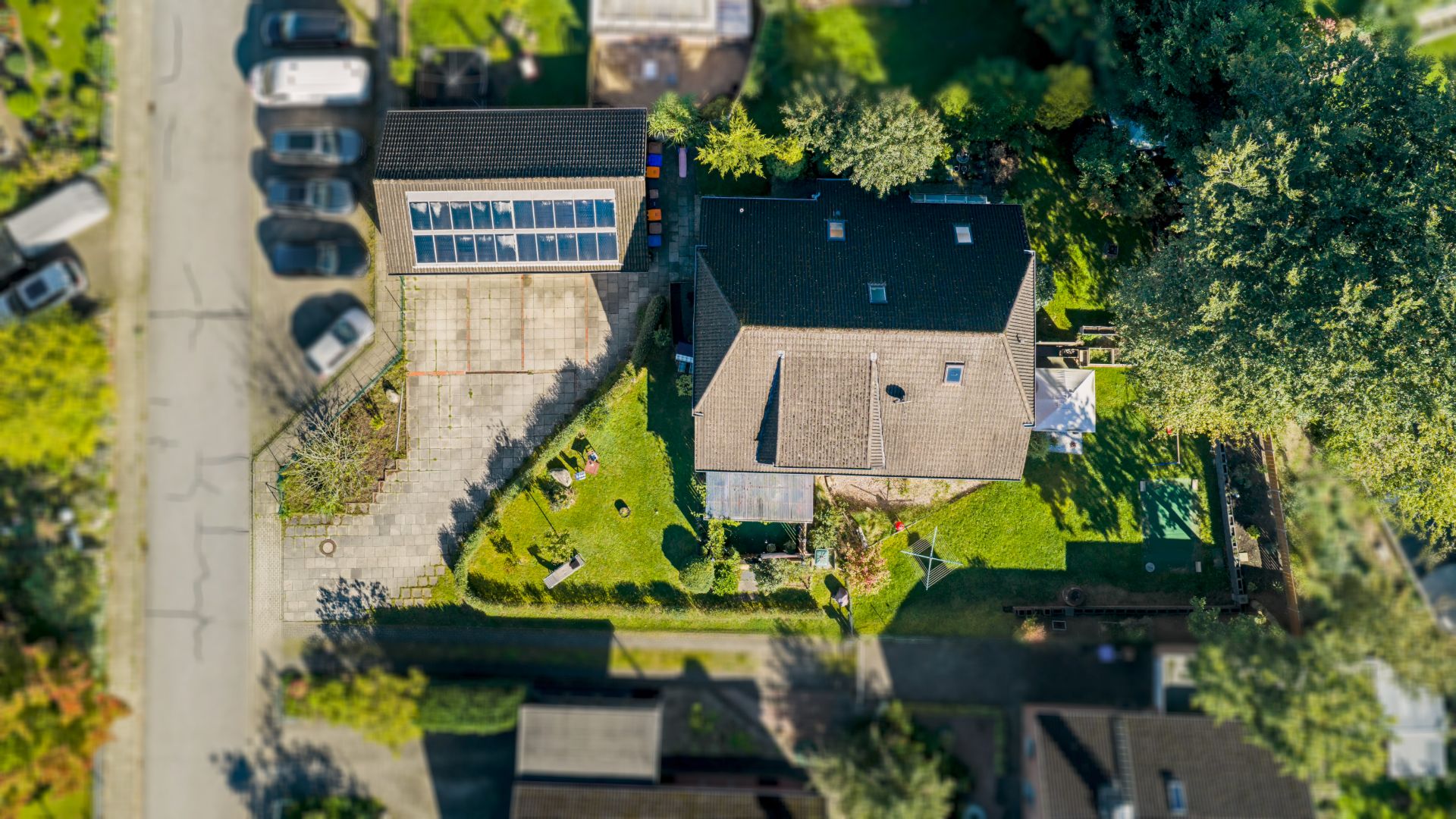 Luftaufnahme eines Hauses mit Garten, Auffahrt und mehreren geparkten Autos an einer Straße.