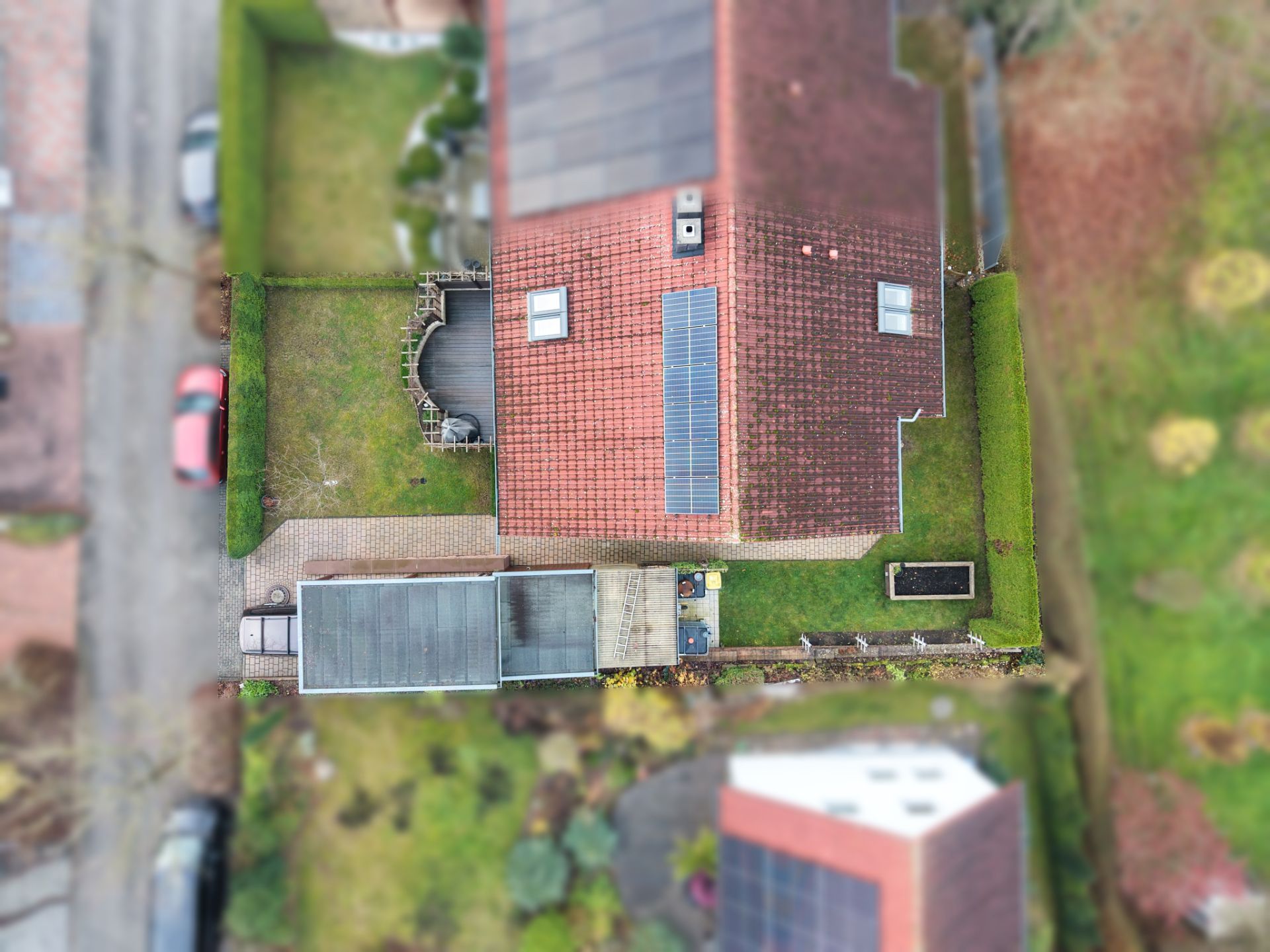 Luftaufnahme eines Hauses mit rotem Dach und Solarpanels, umgeben von Garten und Hecken.