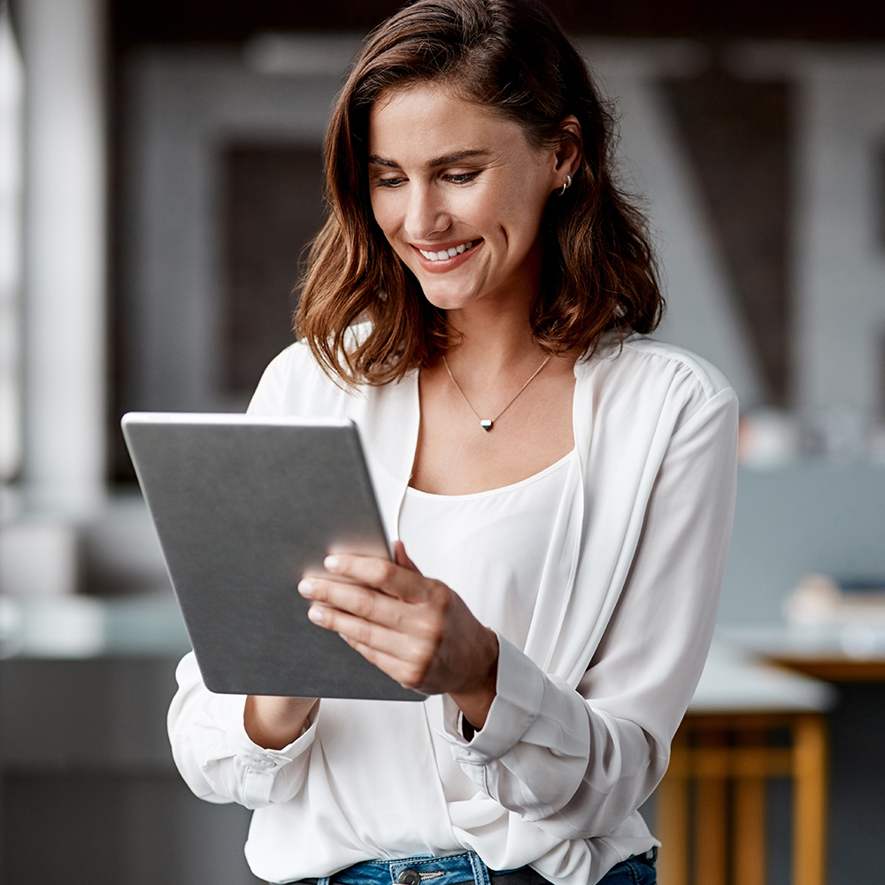 Frau mit braunen Haaren liest auf einem Tablet in einem modernen Raum.