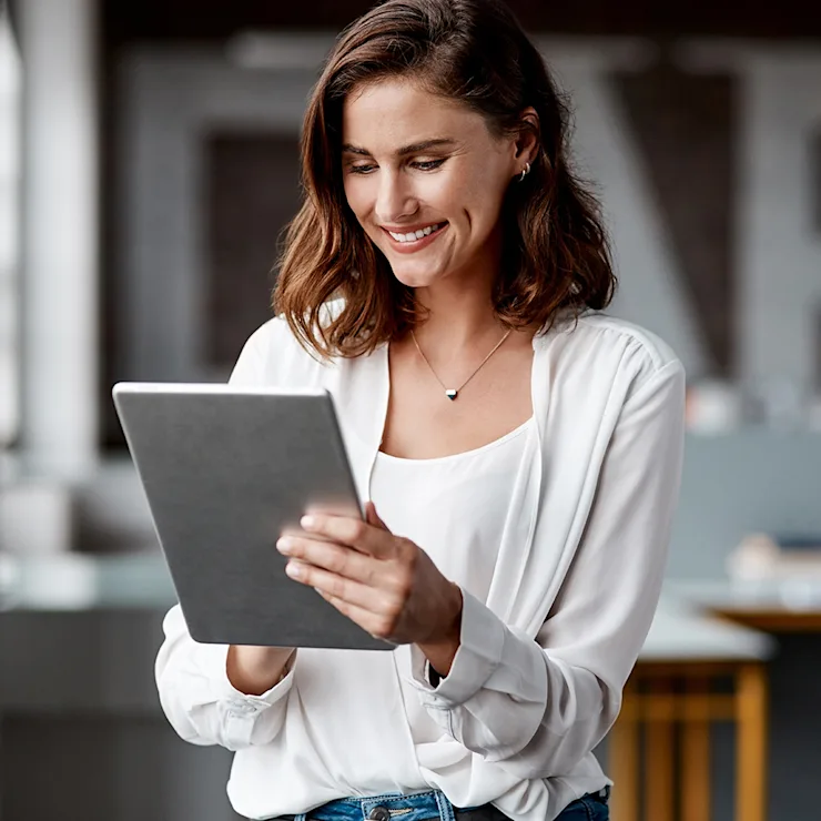 Frau mit braunen Haaren liest auf einem Tablet in einem modernen Raum.