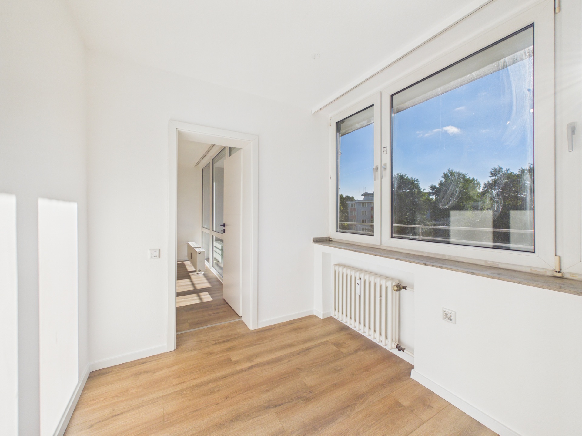 Heller Raum mit Holzboden, großen Fenstern und Heizkörper unter dem Fenster.