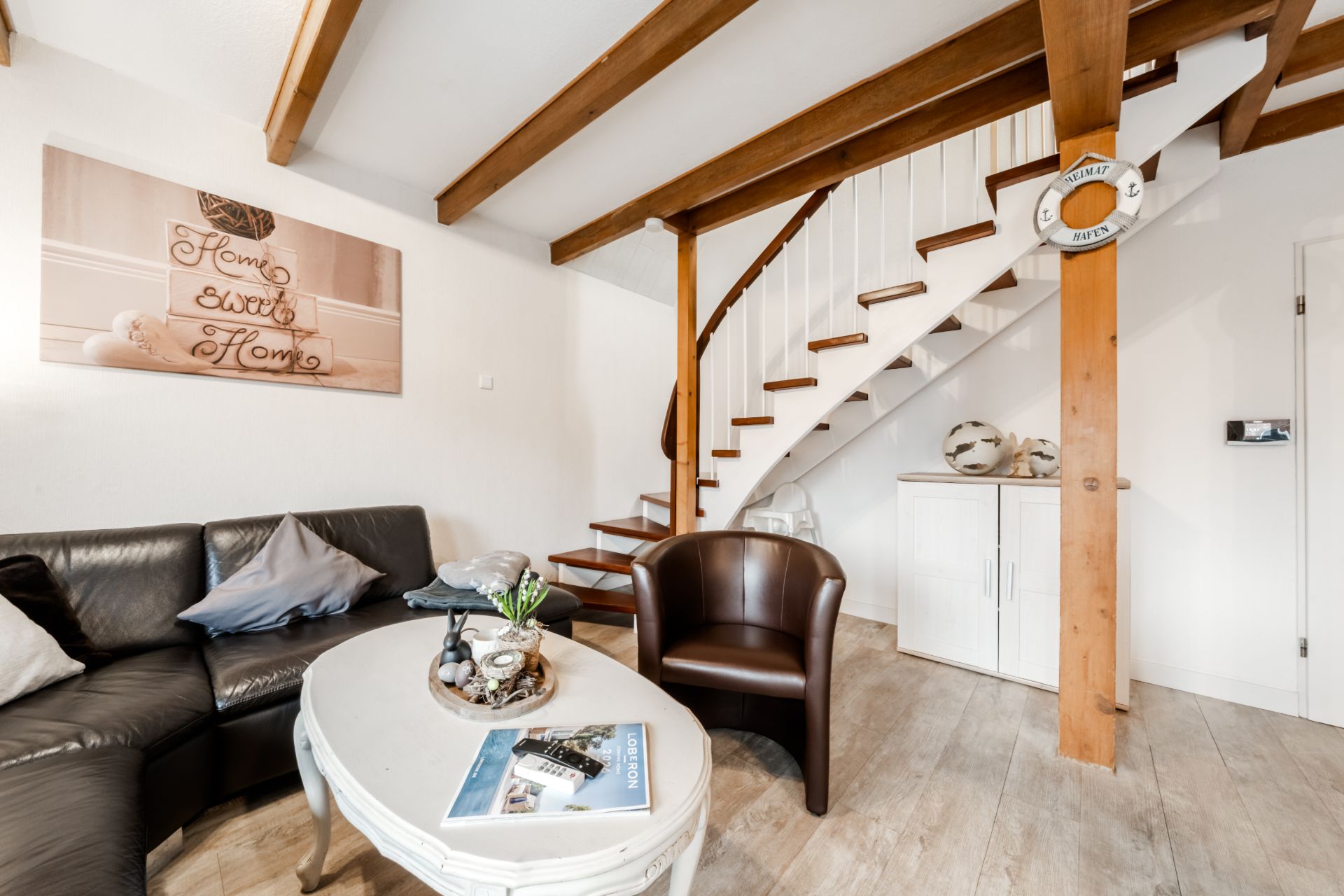 Wohnzimmer mit Sofa, Sessel, Couchtisch und offener Holztreppe.