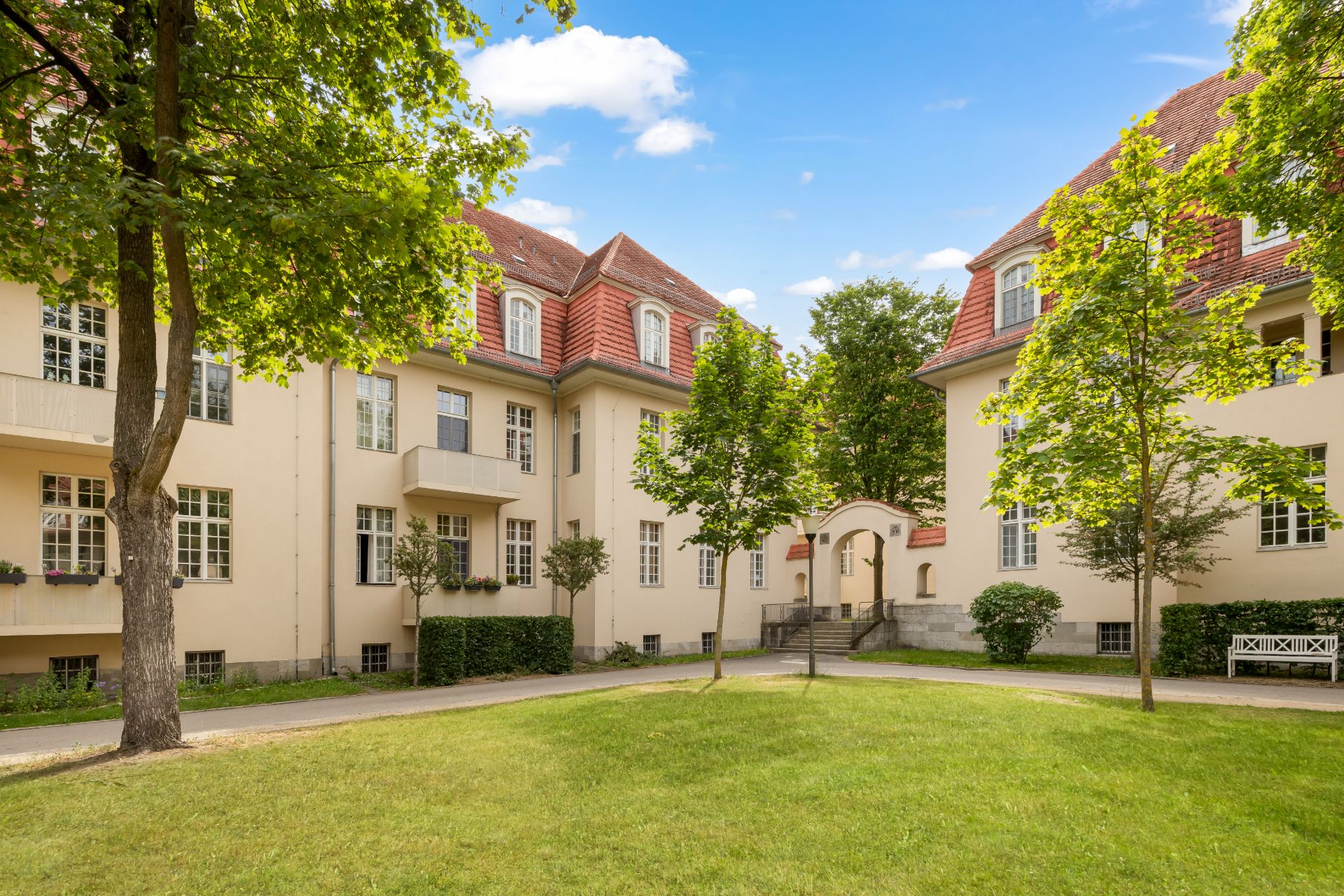 Innenhof mit Rasenfläche, Bäumen und hellen Wohngebäuden mit roten Dächern.