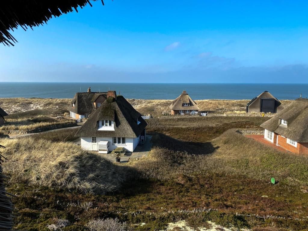 Reetgedeckte Häuser stehen in einer Dünenlandschaft mit Blick auf das Meer.