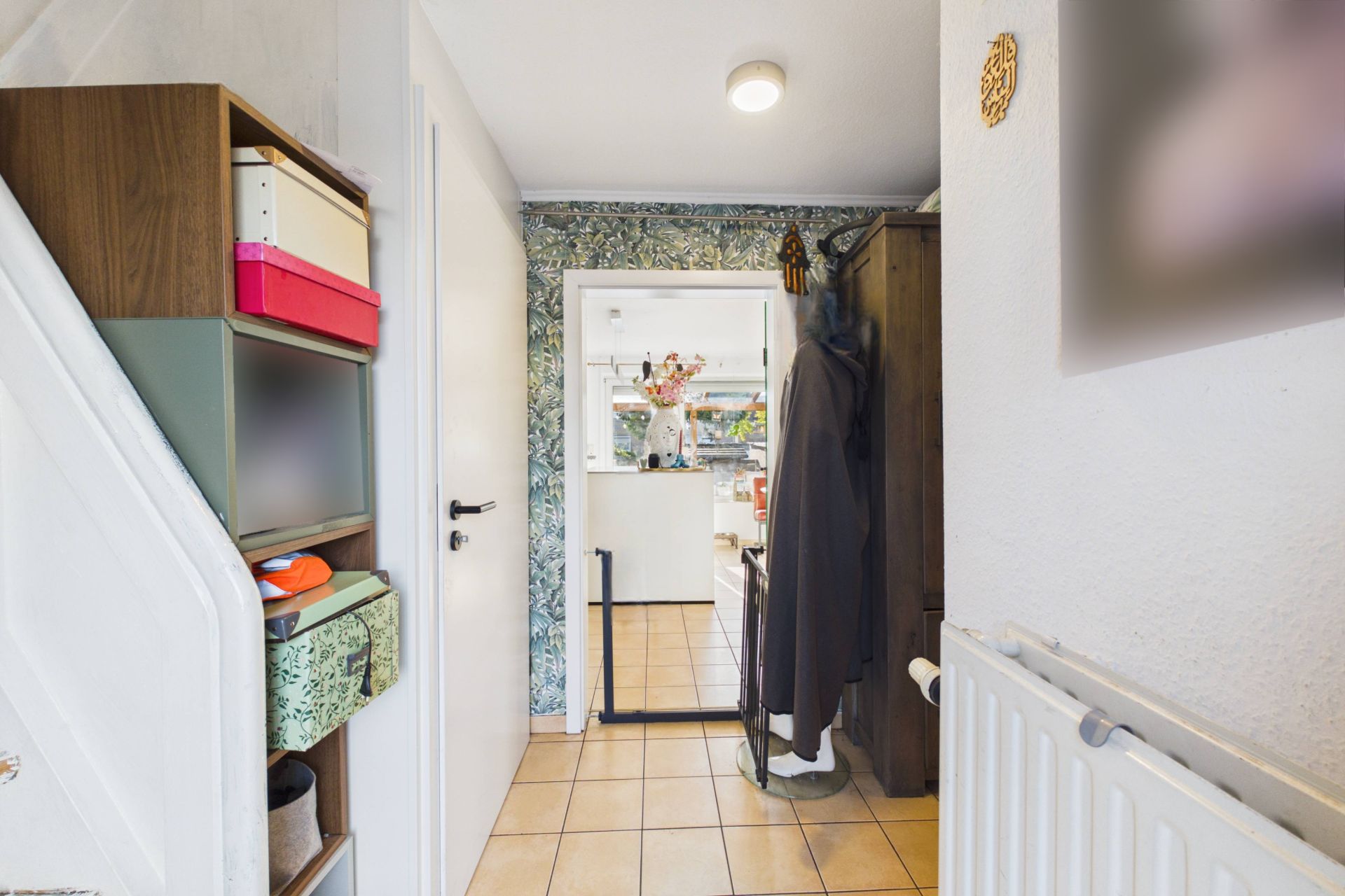 Flur mit Regal, Garderobe und Blick in eine helle Küche mit Fliesenboden.