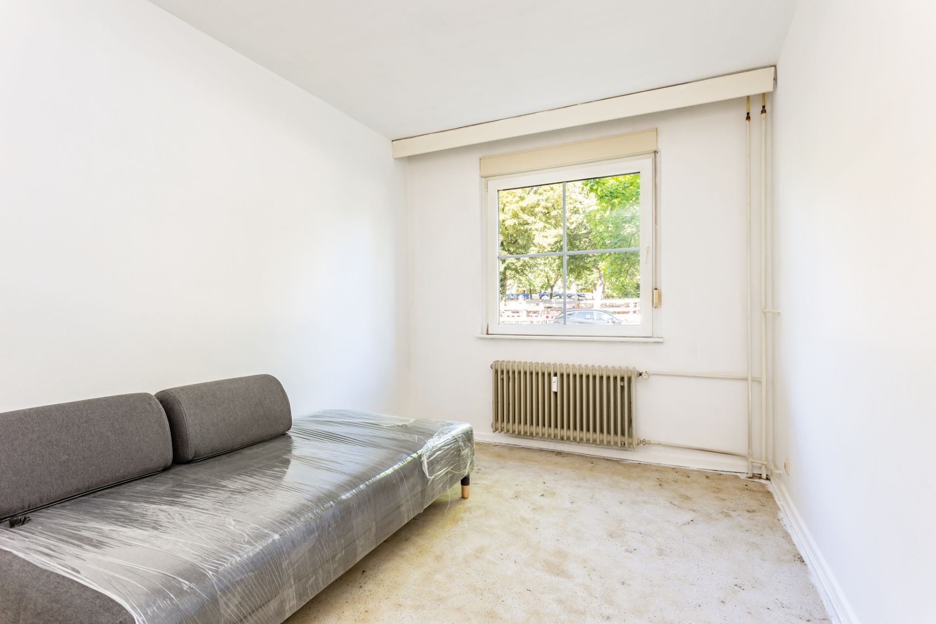 Heller Raum mit einem grauen Sofa, Fenster und Heizkörper unter dem Fenster.