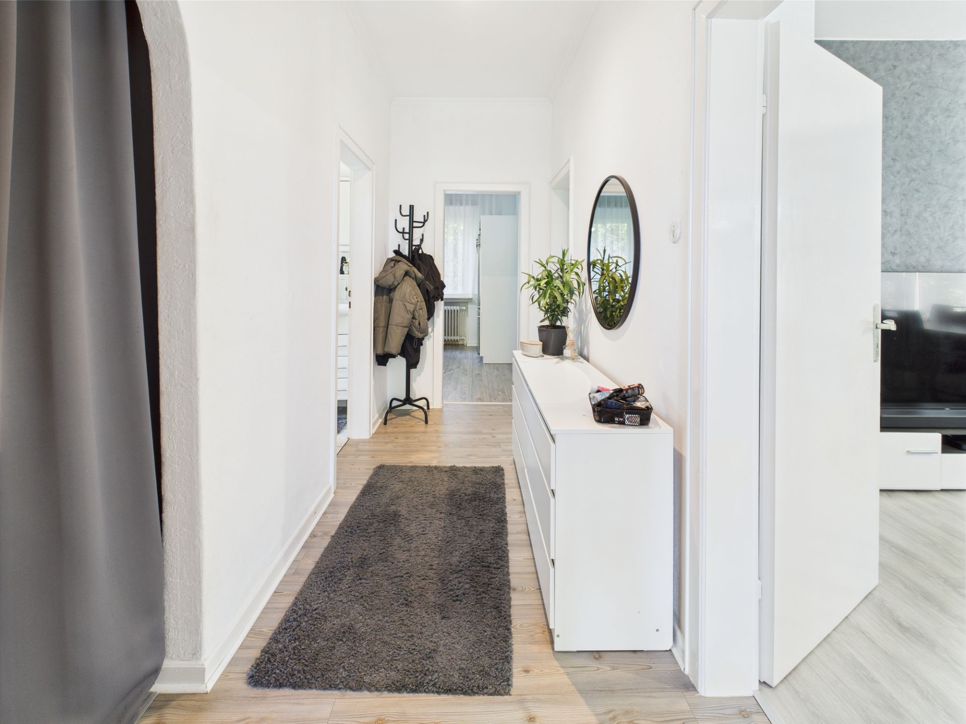 Heller Flur mit Teppich, Kommode, Spiegel und Garderobe mit Jacken.