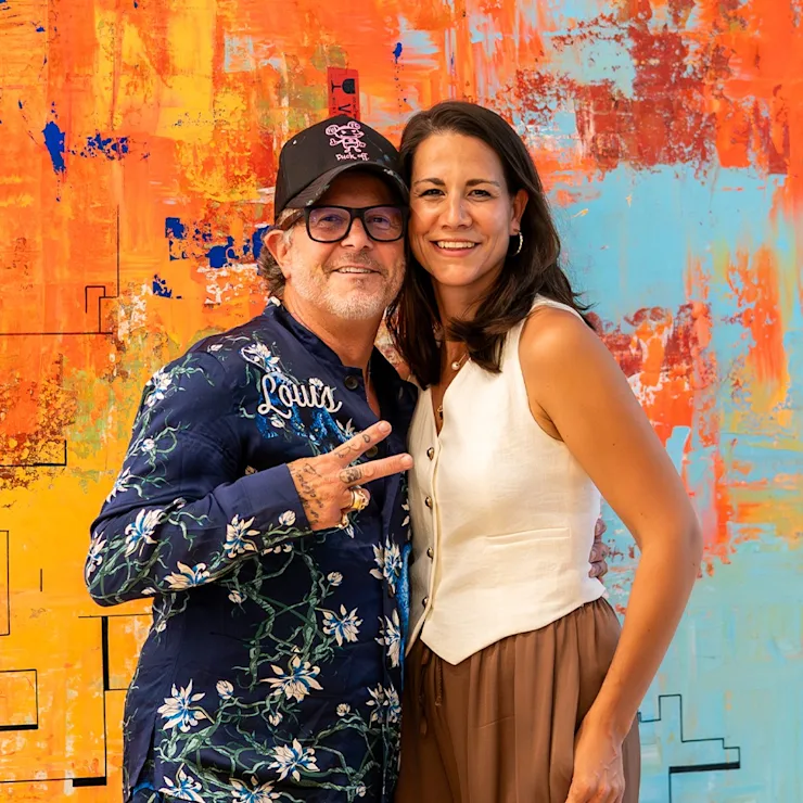 Ein Mann und eine Frau stehen lächelnd vor einem bunten Kunstwerk.