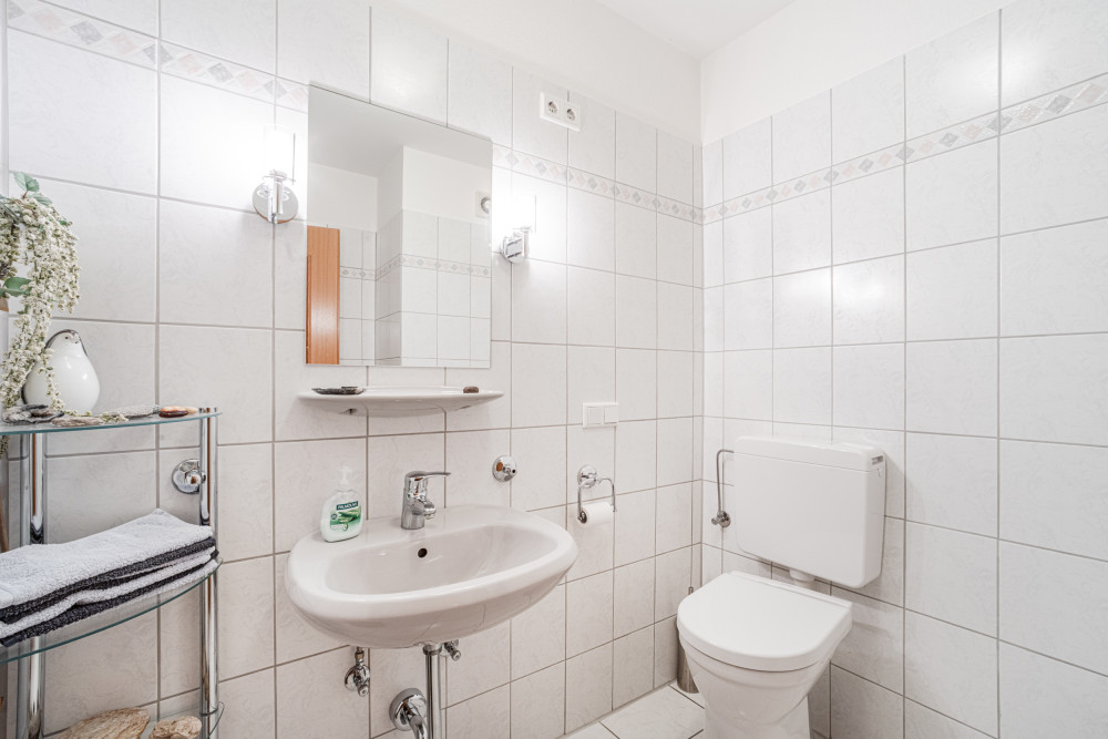 Helles Badezimmer mit Waschbecken, Spiegel, Toilette und Regal mit Handtüchern.