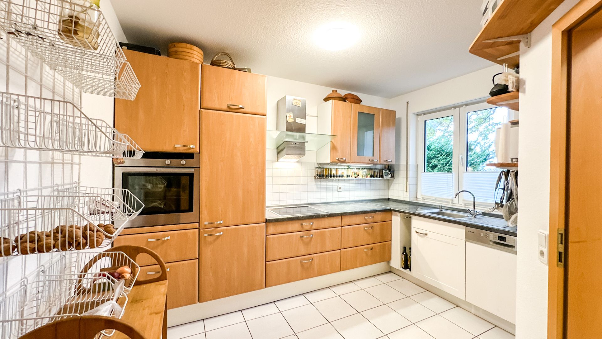 Moderne Einbauküche mit Holzfronten, Backofen, Spülmaschine und großem Fenster.