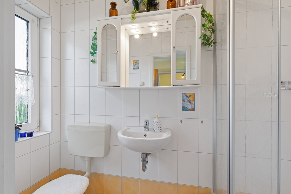 Helles Badezimmer mit WC, Waschbecken, Spiegelschrank und Fenster.