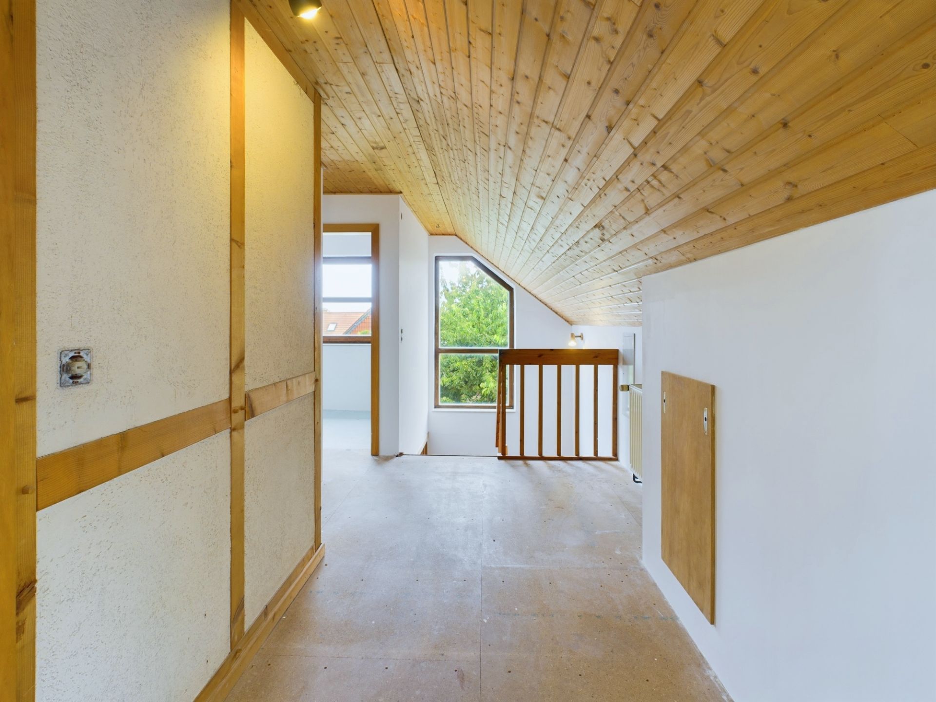 Dachgeschossflur mit Holzdecke, Fenster und Treppengeländer, helle Wände.