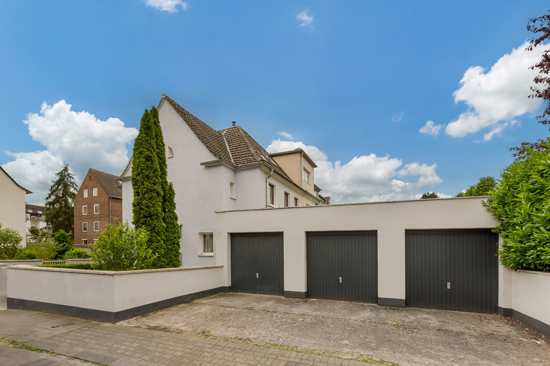 Weiße Wohnhaus-Fassade mit drei Garagentoren und grünem Baum im Vordergrund.