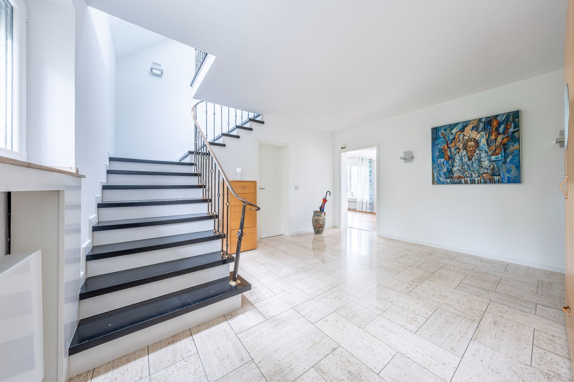 Heller Flur mit Treppe, hellem Boden, Gemälde an der Wand und großem Fenster.