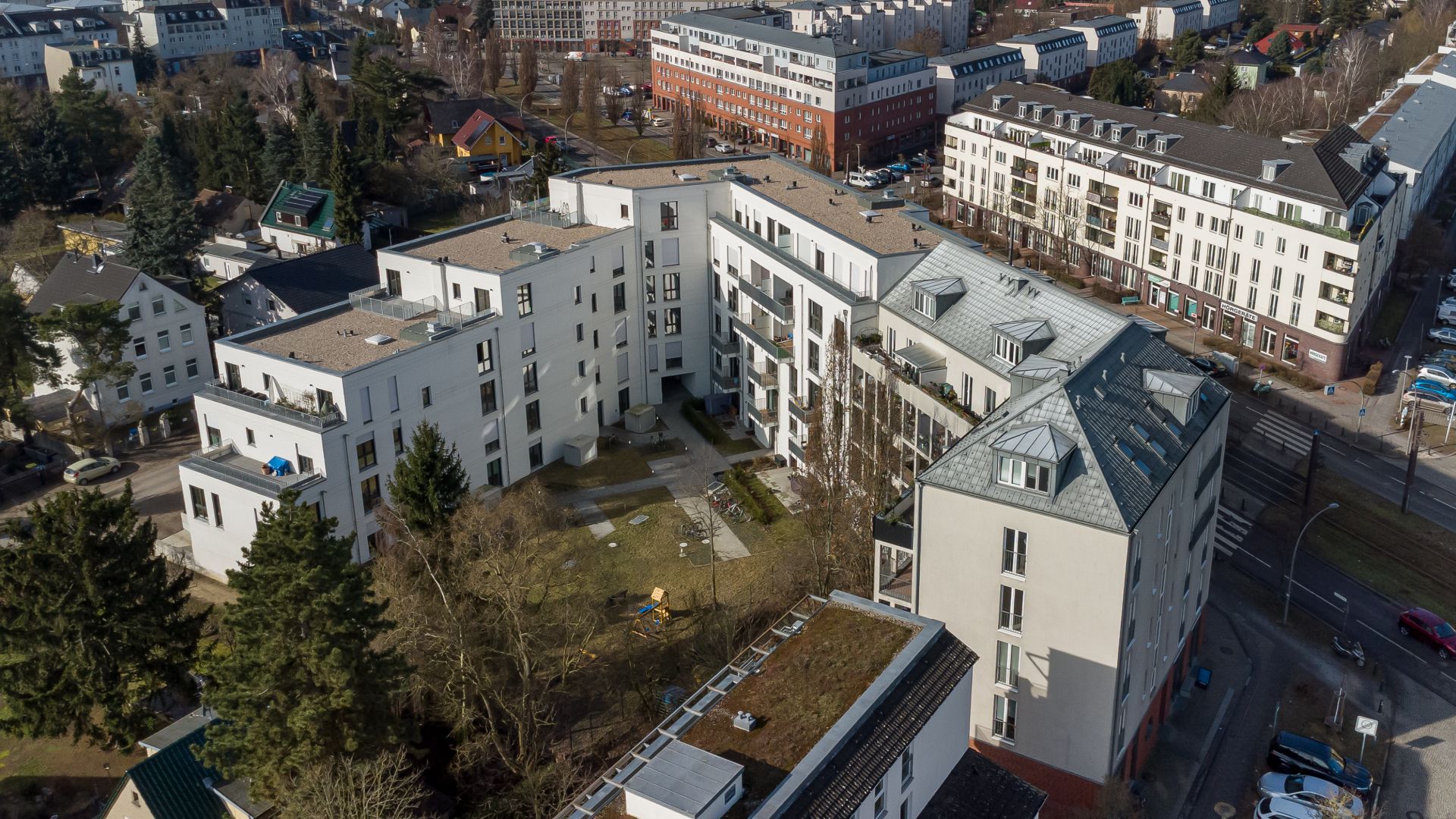 Luftaufnahme eines modernen Wohngebäudekomplexes mit Innenhof und umliegenden Straßen.