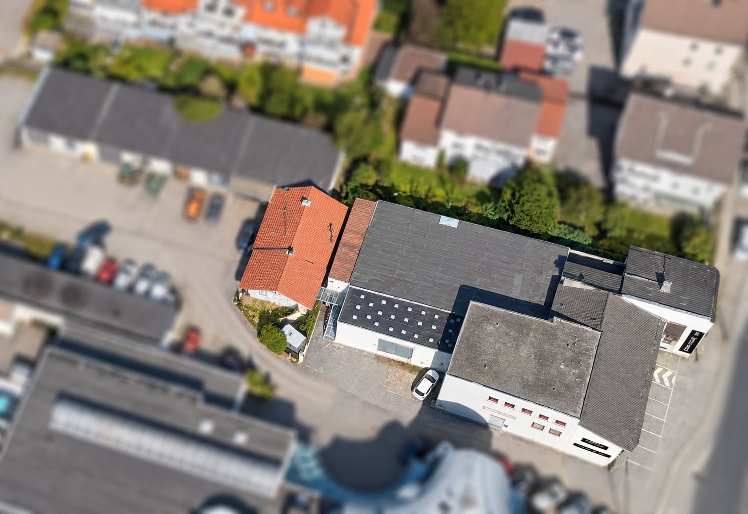 Luftbild von Gebäuden mit roten und grauen Dächern, umgeben von Straßen und geparkten Autos.