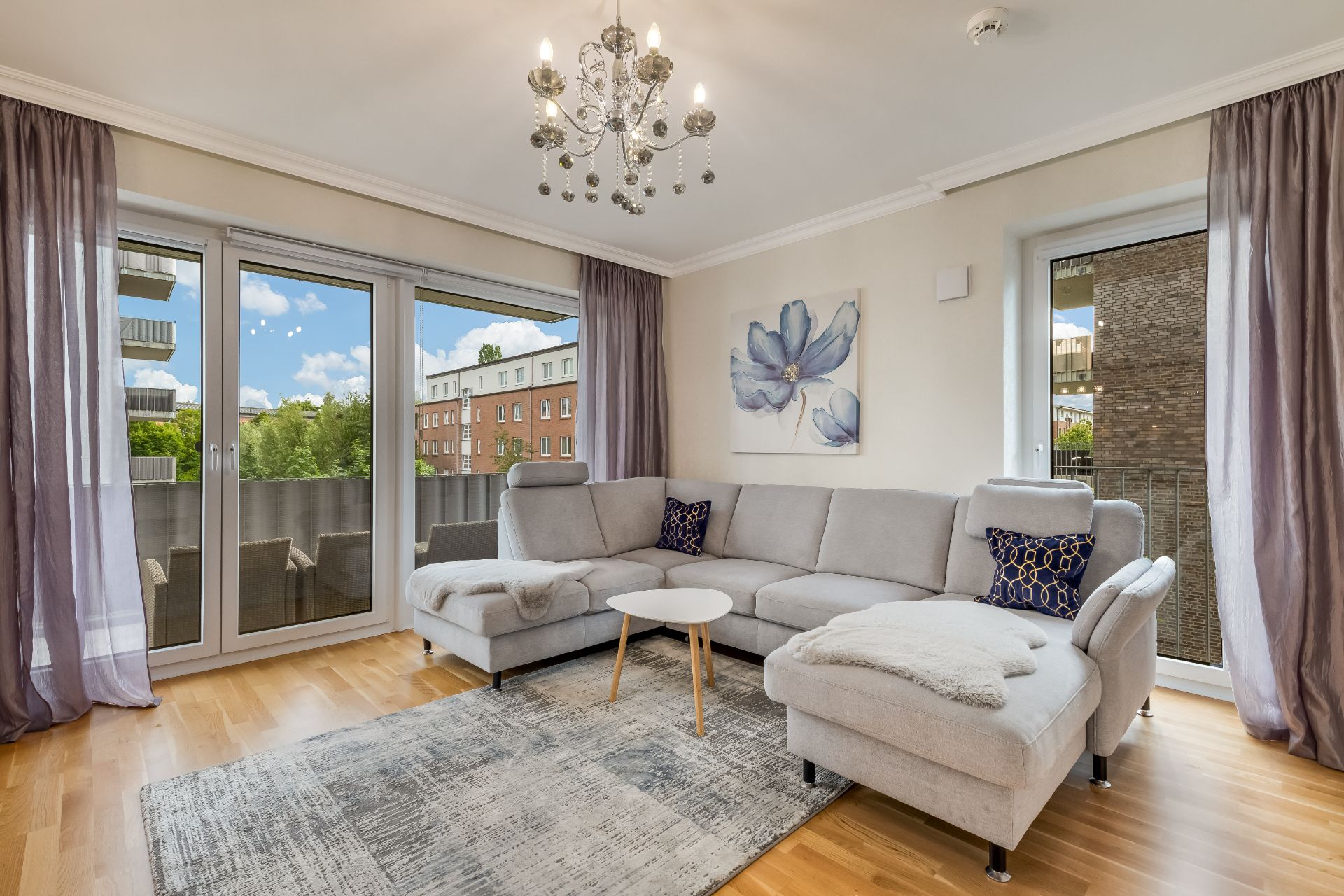 Helles Wohnzimmer mit grauem Ecksofa, Teppich, Couchtisch und großem Fenster.