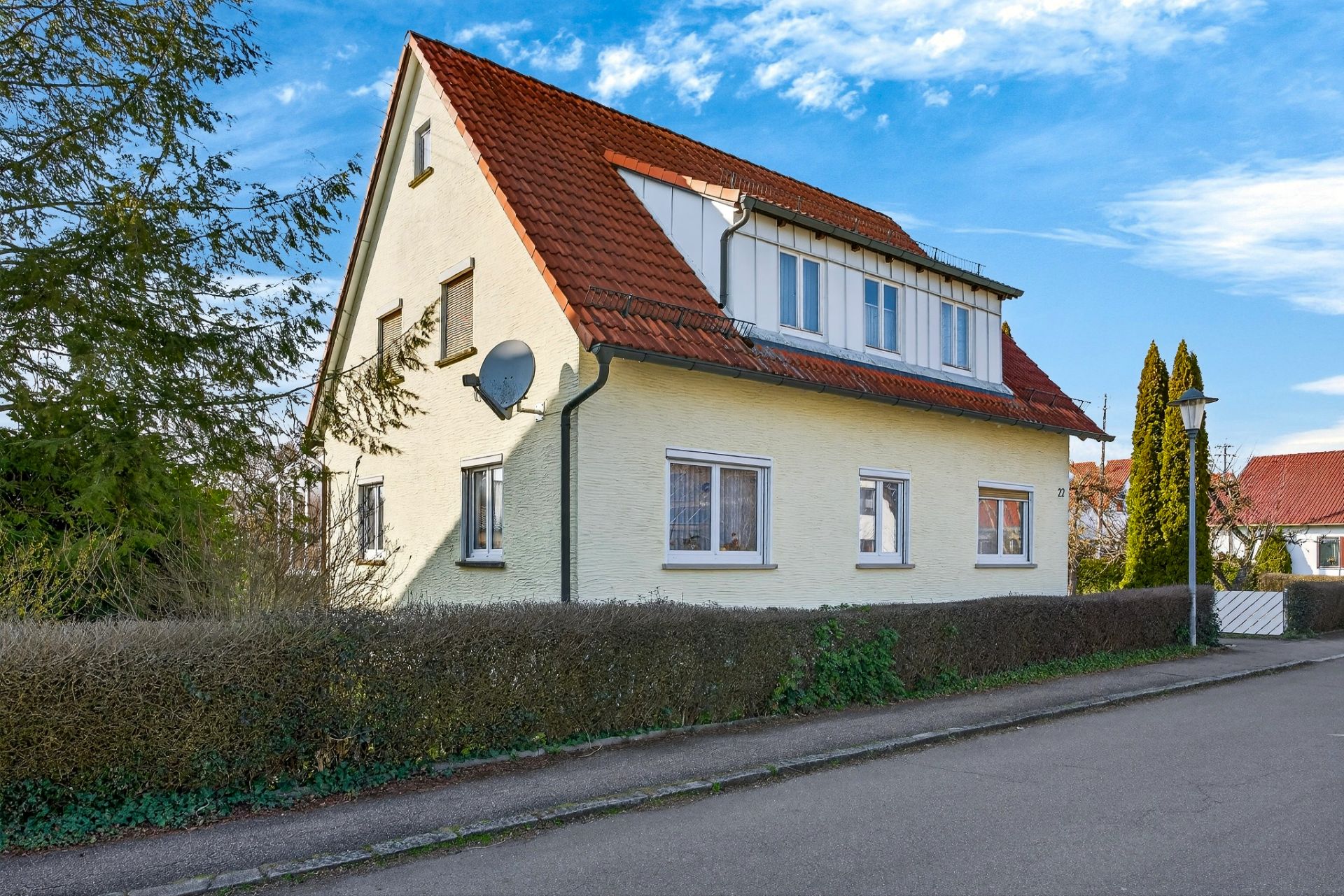 Zweistöckiges Wohnhaus mit rotem Dach und gelber Fassade an einer ruhigen Straße.