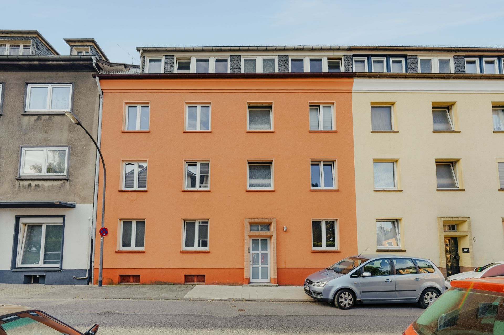 Orangefarbenes Mehrfamilienhaus mit mehreren Fenstern und geparkten Autos davor.