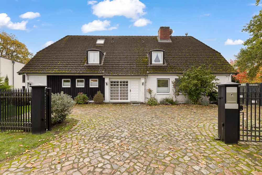 Zweistöckiges Wohnhaus mit dunklem Dach, Einfahrt mit Kopfsteinpflaster und Gartentor.