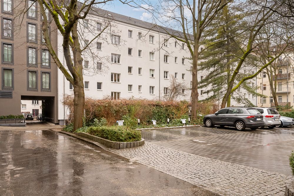 Wohnhaus mit Parkplatz, mehreren Autos und Bäumen im Vordergrund.
