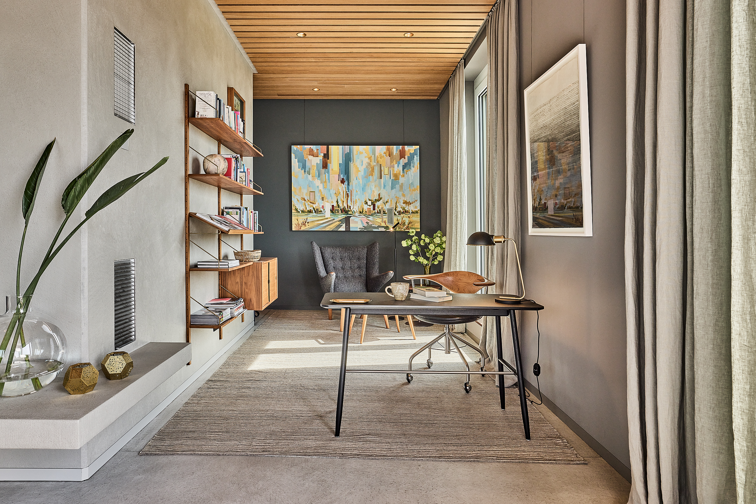 Modernes Arbeitszimmer mit Schreibtisch, Regal, Sessel und bunter Wandkunst.
