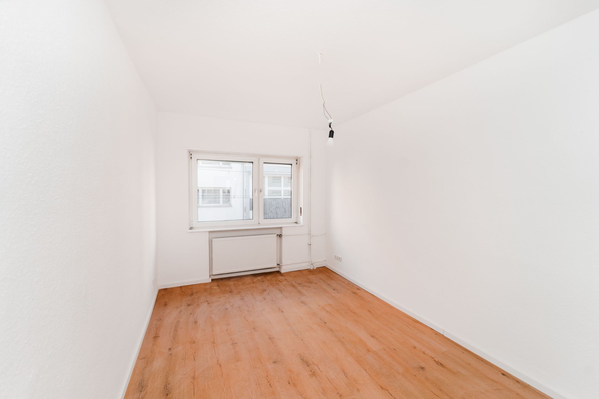 Leerer Raum mit weiß gestrichenen Wänden, Fenster und Holzfußboden.
