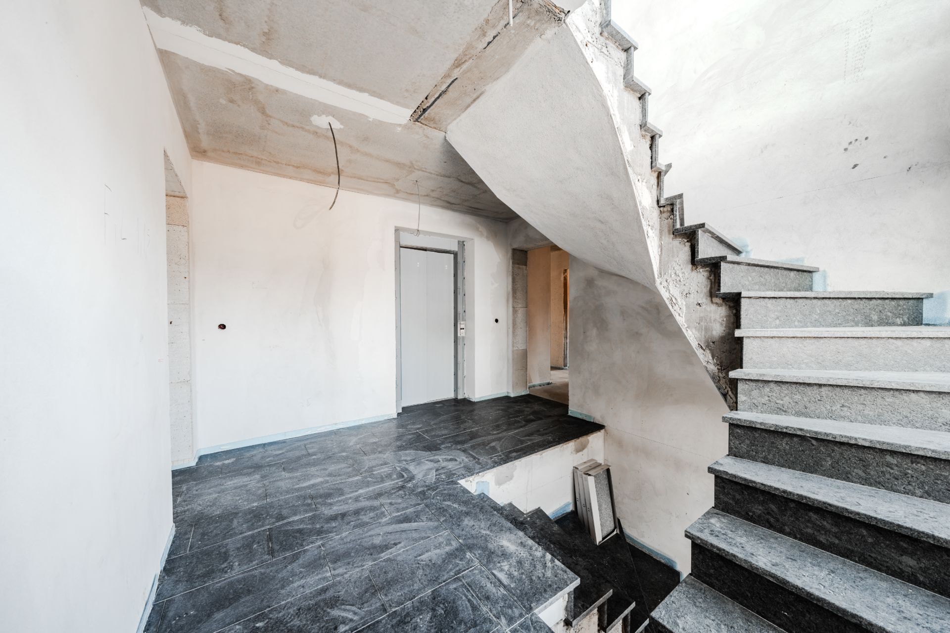 Treppenhaus mit grauen Fliesen und unverputzten Wänden in einem Wohngebäude.