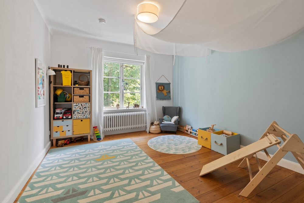 Kinderzimmer mit Teppich, Regalen, Spielzeug, Sessel und Rutsche auf Holzboden.