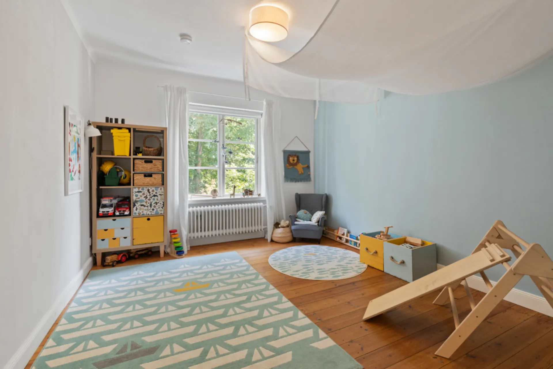 Kinderzimmer mit Teppich, Regalen, Spielzeug, Sessel und Rutsche auf Holzboden.
