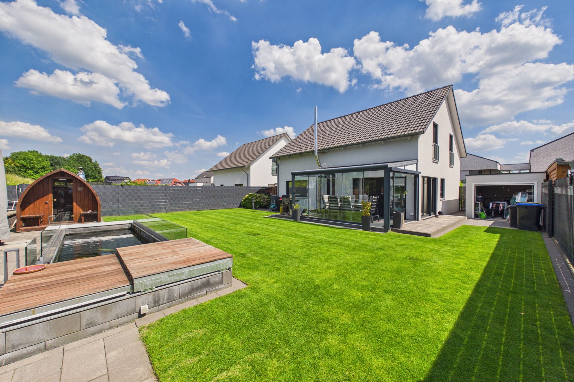 Modernes Einfamilienhaus mit Wintergarten, Terrasse, Rasenfläche und kleinem Teich im Garten.