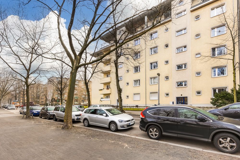 Mehrstöckiges Wohnhaus mit geparkten Autos und kahlen Bäumen an der Straße.