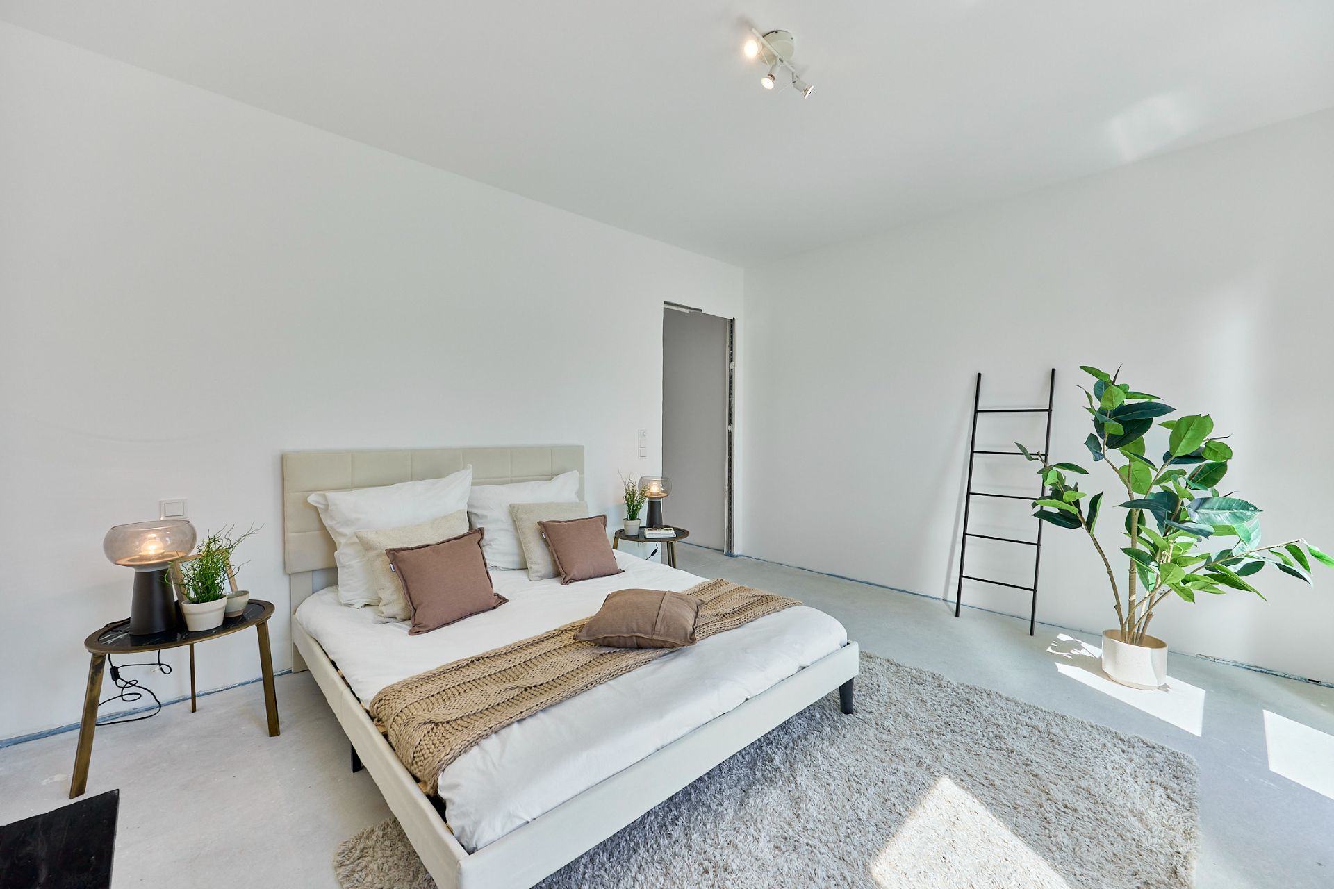 Helles Schlafzimmer mit weißem Bett, Teppich, Pflanzen und Dekoleiter an der Wand.