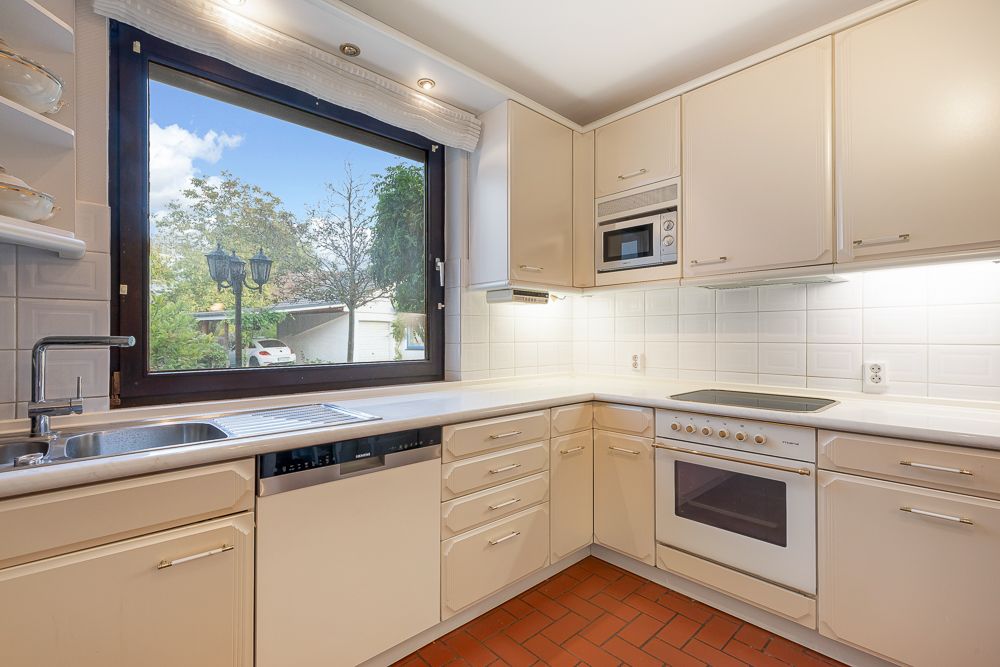 Helle Einbauküche mit großem Fenster, Spüle, Herd, Backofen und weißen Schränken.