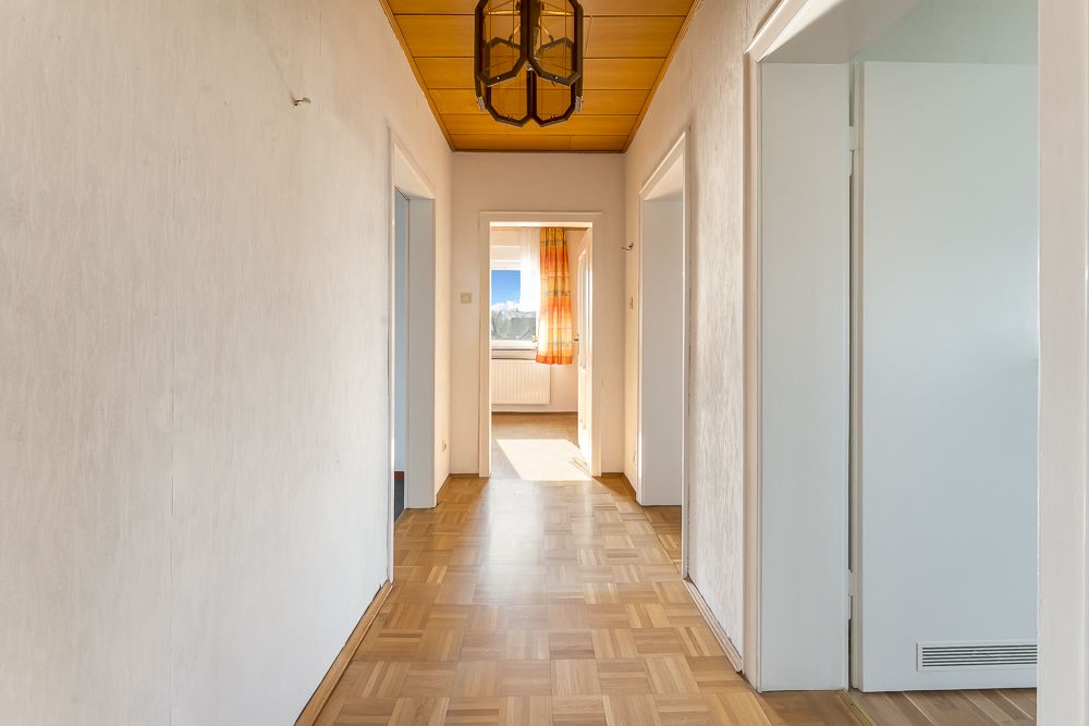 Heller Flur mit Parkettboden, Holzdecke und mehreren offenen Türen, Tageslicht am Ende.