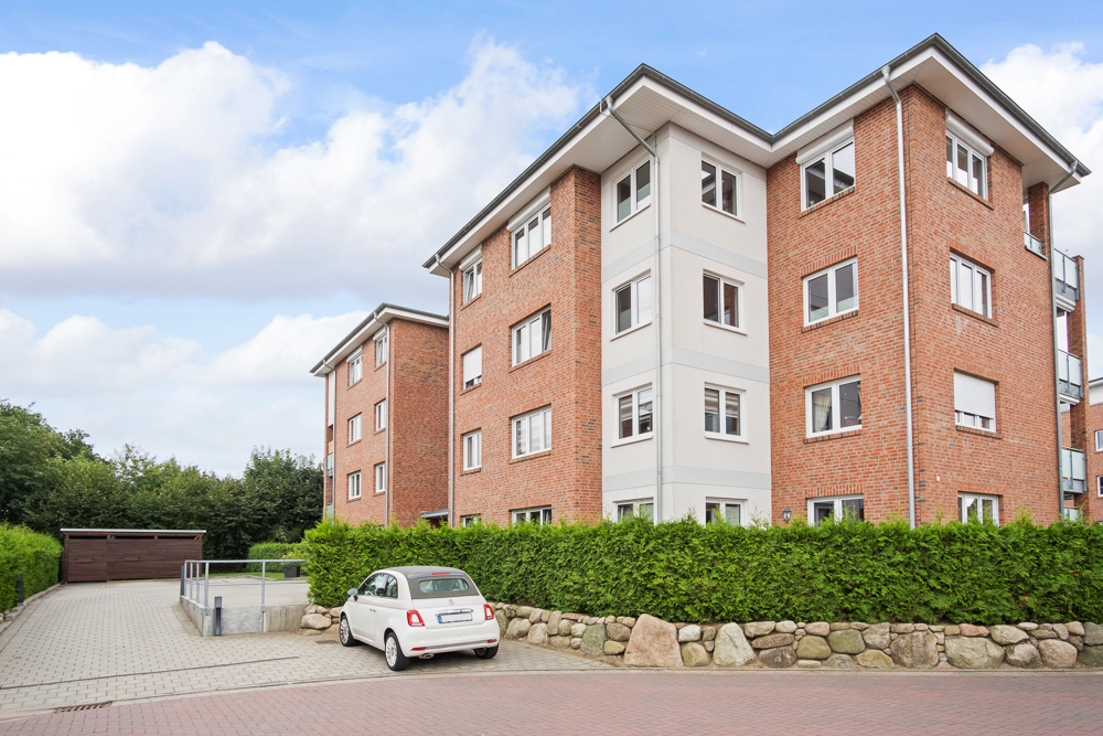 Mehrfamilienhaus aus rotem Klinker mit weißen Fenstern, davor steht ein weißes Auto.