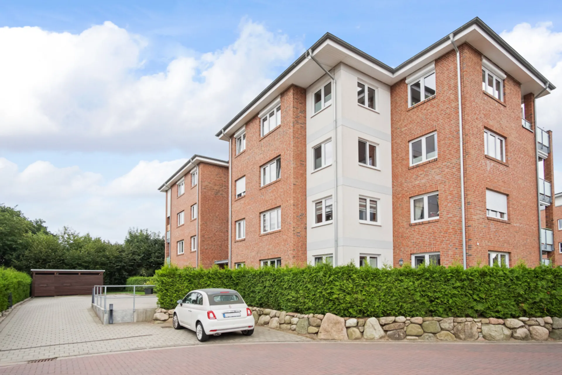 Mehrfamilienhaus aus rotem Klinker mit weißen Fenstern, davor steht ein weißes Auto.
