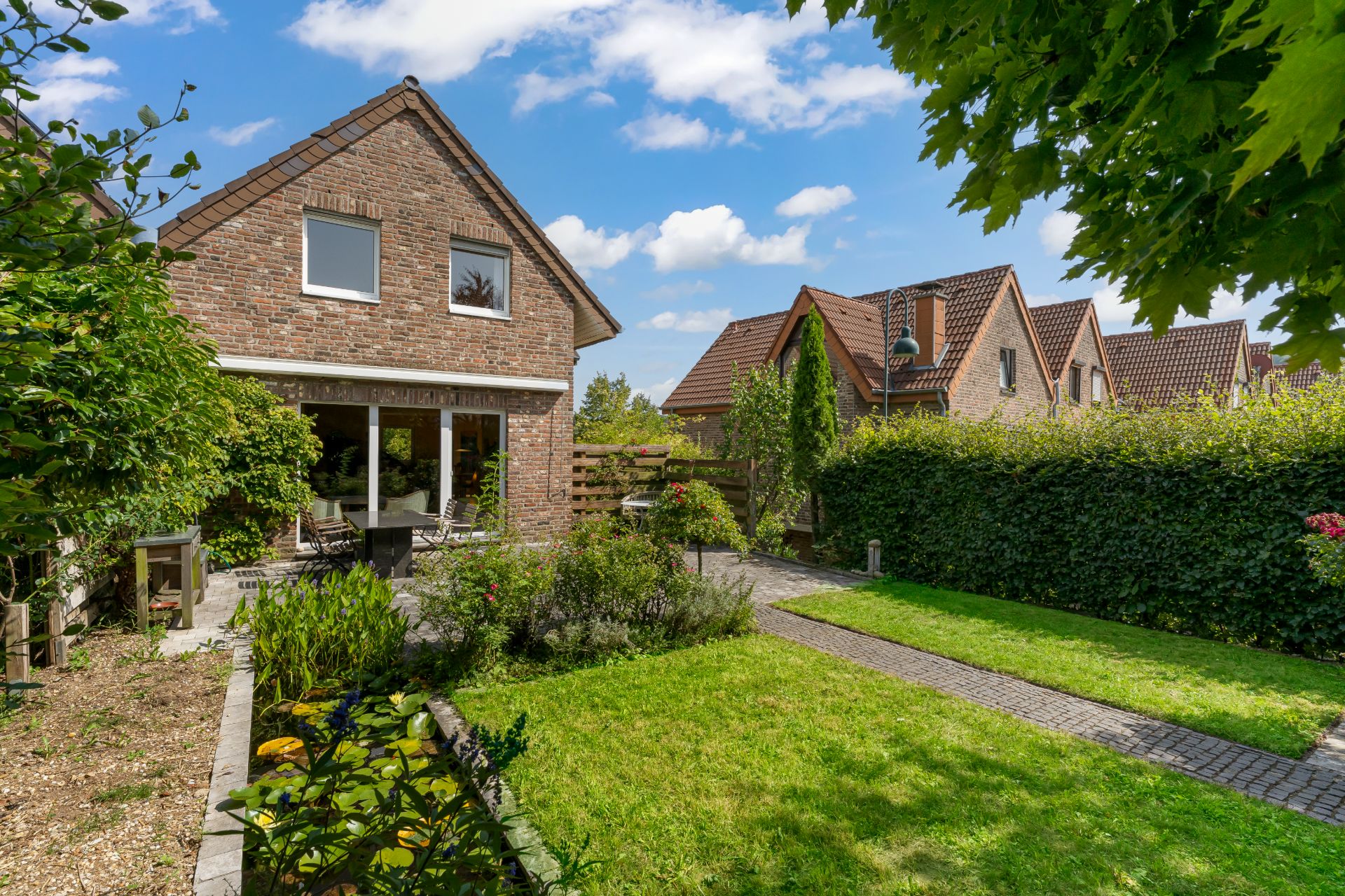 Backsteinwohnhaus mit großem Garten, Rasenfläche und Terrasse bei sonnigem Wetter.