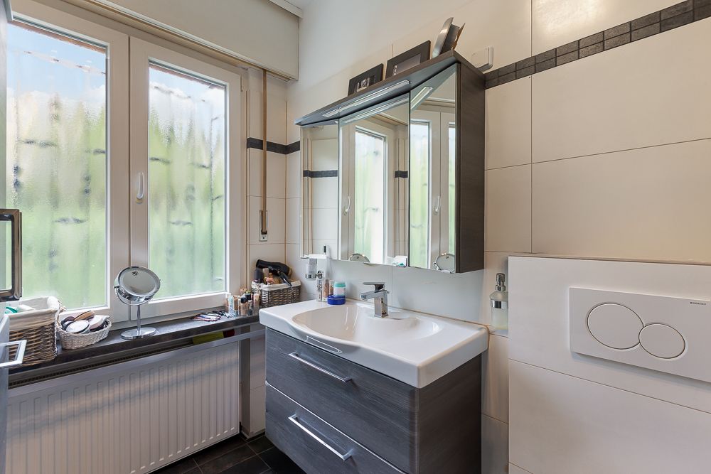 Modernes Badezimmer mit Waschbecken, Spiegel­schrank und Fenster.