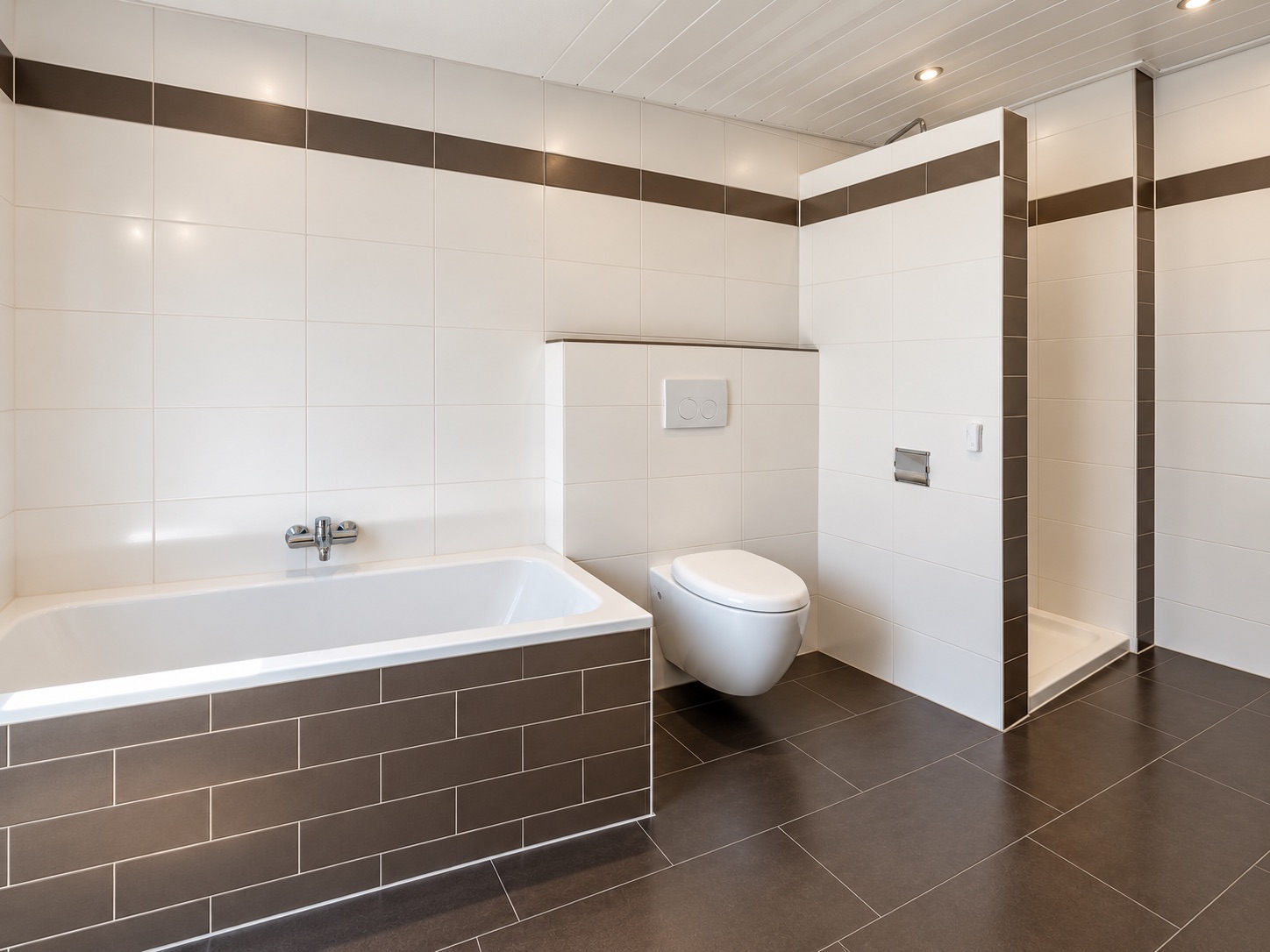 Modernes Badezimmer mit Badewanne, Toilette und offener Dusche, weiß-braune Fliesen.