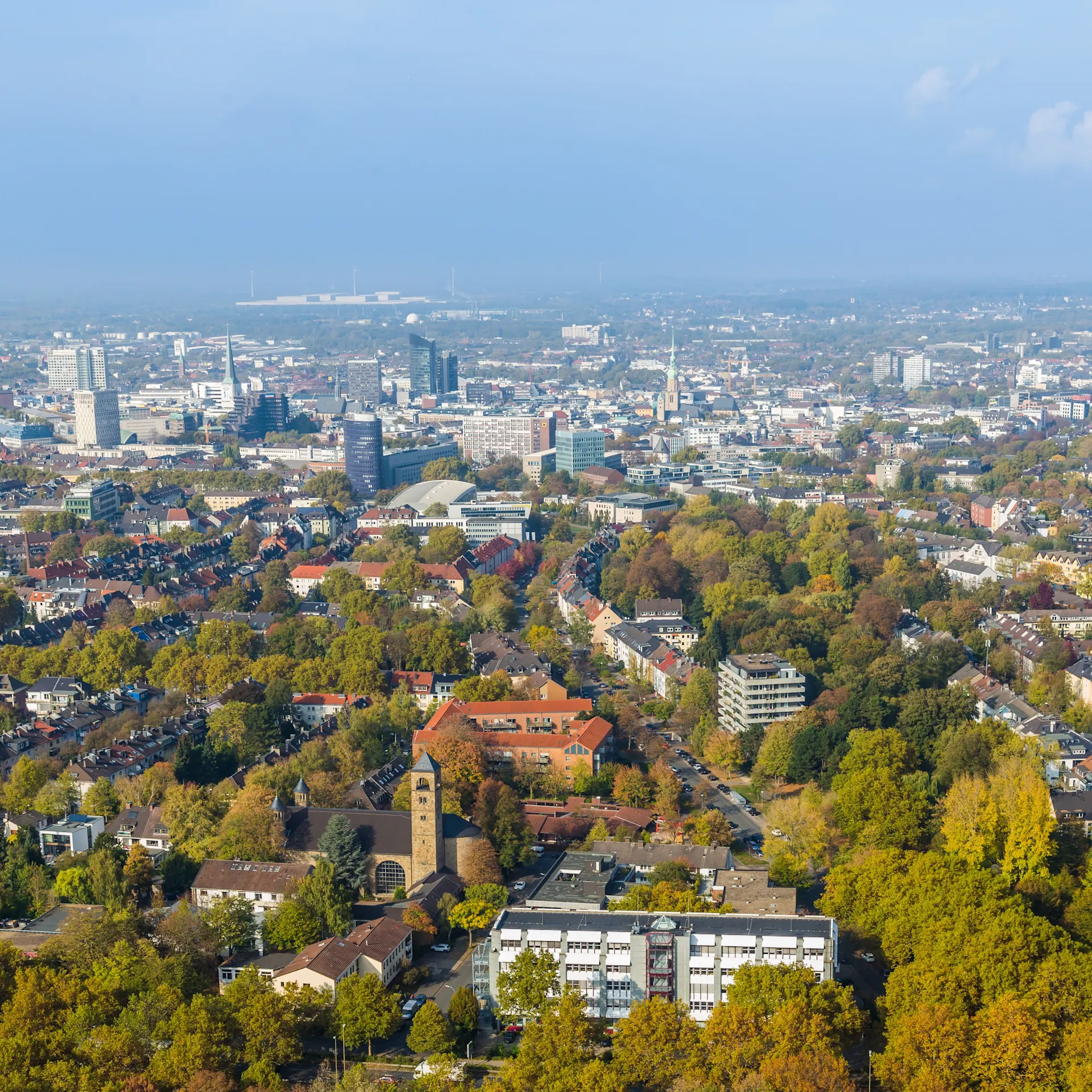 Luftaufnahme einer Stadt mit vielen Gebäuden und Bäumen im Vordergrund.